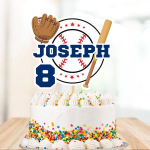 Puede incluir: Un pastel blanco con chispas de colores y un adorno de pastel con temática de béisbol. El adorno presenta una pelota de béisbol, un bate, un guante y el nombre "JOSEPH" con el número "8" en azul.