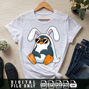 May include: White t-shirt with a graphic of a penguin wearing bunny ears and sunglasses. The penguin is wearing a white scarf and has orange feet.