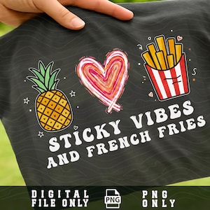 Op de afbeelding: Zwart T-shirt met een ananas, een hart en een bakje friet. De tekst luidt "Sticky Vibes and French Fries". De ananas is geel met een groene bovenkant. Het hart is rood, oranje en roze.