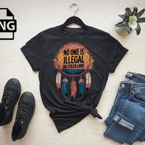 May include: Black t-shirt with a graphic of a dreamcatcher with the text "No one is illegal on stolen land".