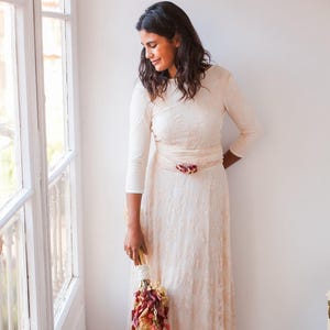 The model is wearing a wedding dress with three-quarter sleeves. She is holding a bouquet full of red flowers that easily combines with her rose quartz lace bridal gown