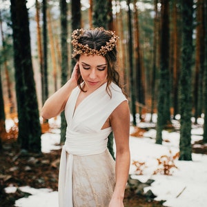 Woman wearing a fall wedding gown in the woods. It's a bit snowy. The woman is wearing a flowery headband that combines perfectly with her bridal gown in ivory and golden