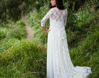 Könnte beinhalten: Ein bodenlanges weißes Kleid mit dreiviertellangen Spitzenärmeln, einem transparenten Spitzeneinsatz am Rücken und einer langen Spitzenschleppe, die mit einem Band an der Taille befestigt ist. Das Kleid hat einen schlichten weißen Rock.