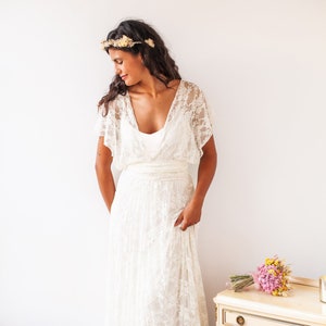 Woman wearing a grecian wedding dress. The lace of the dress is off-white. She has her head slightly turned.