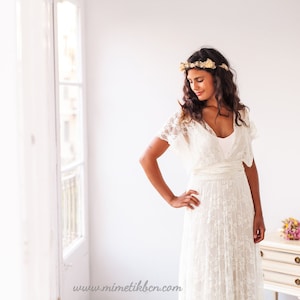 Brunette model in a bright room. She is looking to her left, close to the window. Her skin has a beautiful contrast with the beach wedding dress she is wearing.