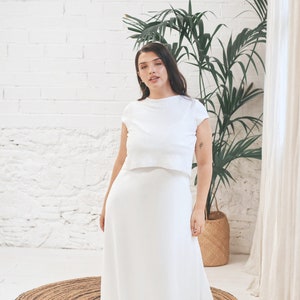 May include: A white, simple, two-piece wedding dress with a short-sleeved top and a long, flowing skirt.