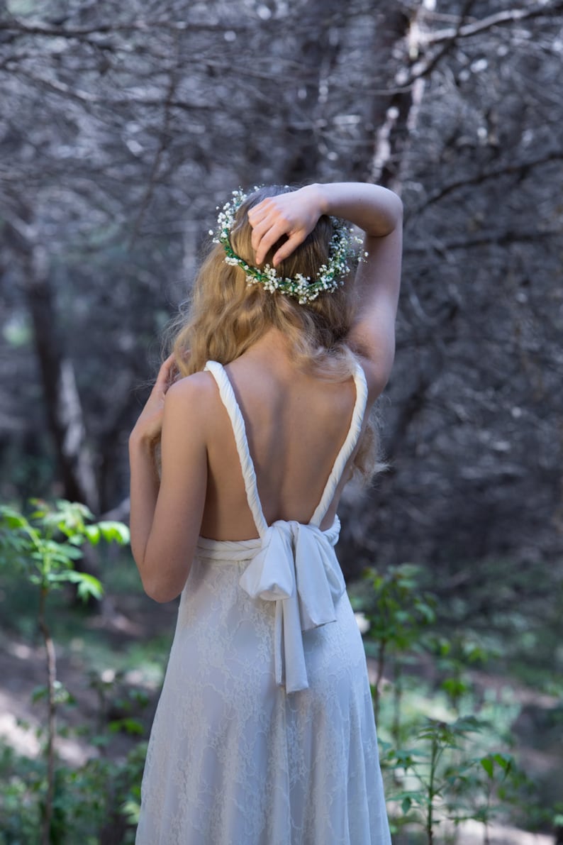 Bride in the woods touching her hair and showing her back.