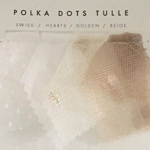 以下が含まれることがあります： POLKA DOTS TULLEと書かれたディスプレイカード。テキストはSWISS / HEARTS / GOLDEN / BEIGE。白、クリーム、ベージュの色合いのシアーなチュール生地のサンプルが5枚並んでおり、小さなドットやハートの模様が入っているものもあります。