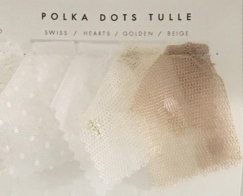 以下が含まれることがあります： POLKA DOTS TULLEと書かれたディスプレイカード。テキストはSWISS / HEARTS / GOLDEN / BEIGE。白、クリーム、ベージュの色合いのシアーなチュール生地のサンプルが5枚並んでおり、小さなドットやハートの模様が入っているものもあります。