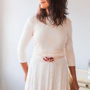 The model is wearing a modest wedding dress. It's perfect for a winter wedding thanks to the three-quarter sleeves. She combines a convertible bridal dress with a lace overskirt