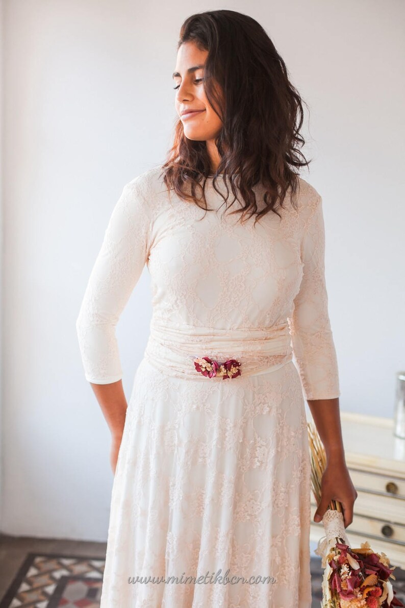 The model is wearing a modest wedding dress. It's perfect for a winter wedding thanks to the three-quarter sleeves. She combines a convertible bridal dress with a lace overskirt