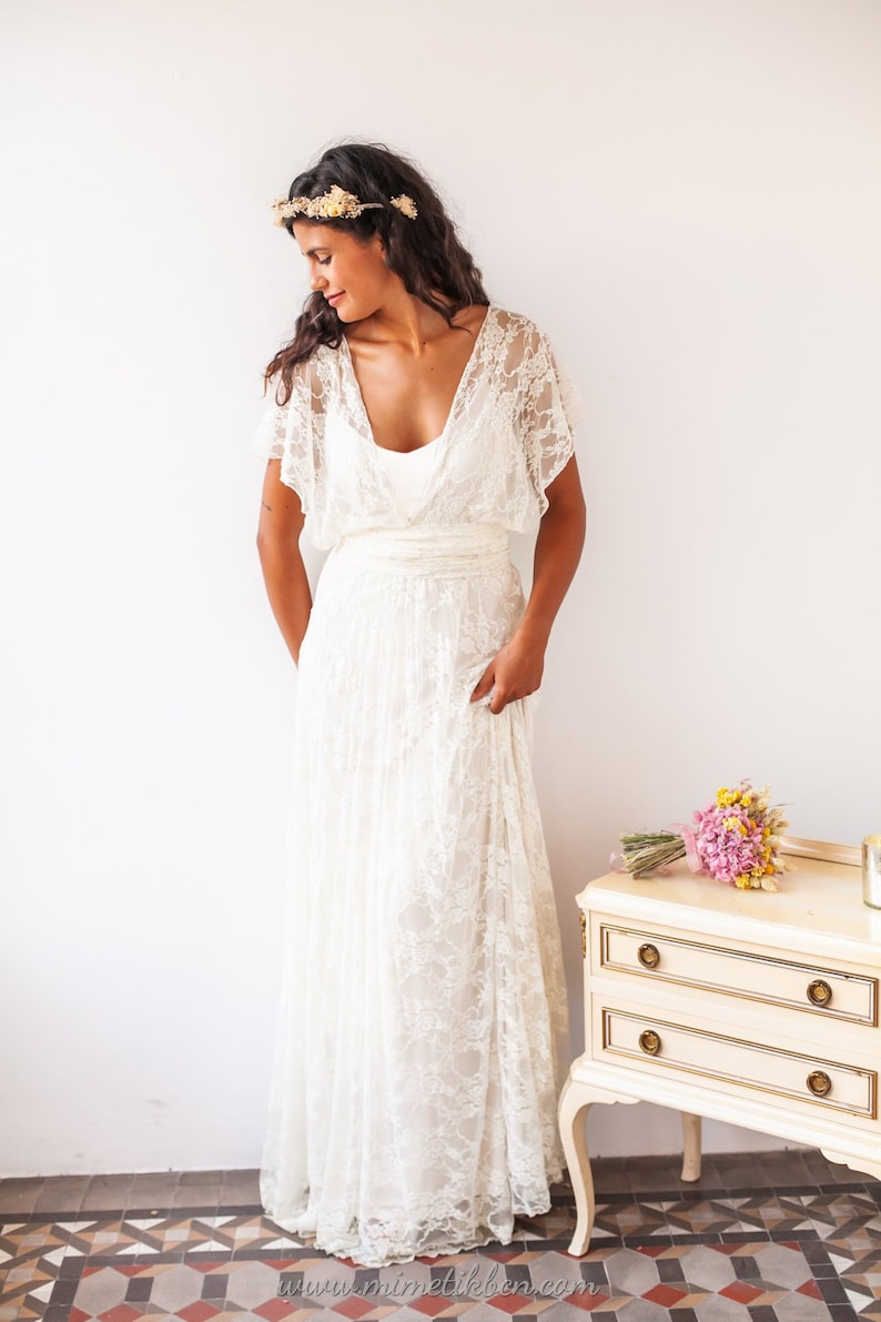 Woman wearing a grecian wedding dress. The lace of the dress is off-white. She has her head slightly turned.