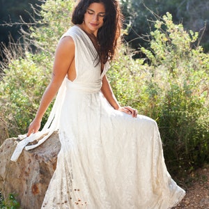 A woman is sitting in a natural rock. She is wearing an elegant and romantic wedding dress. The dress has an ethereal appearence. The dress is full made of ivory satin jersey and ivory lace. The dress is also floor lenght.