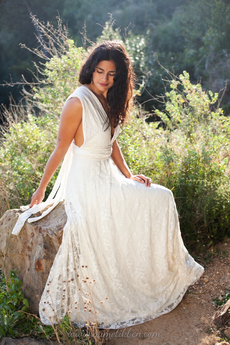 A woman is sitting in a natural rock. She is wearing an elegant and romantic wedding dress. The dress has an ethereal appearence. The dress is full made of ivory satin jersey and ivory lace. The dress is also floor lenght.