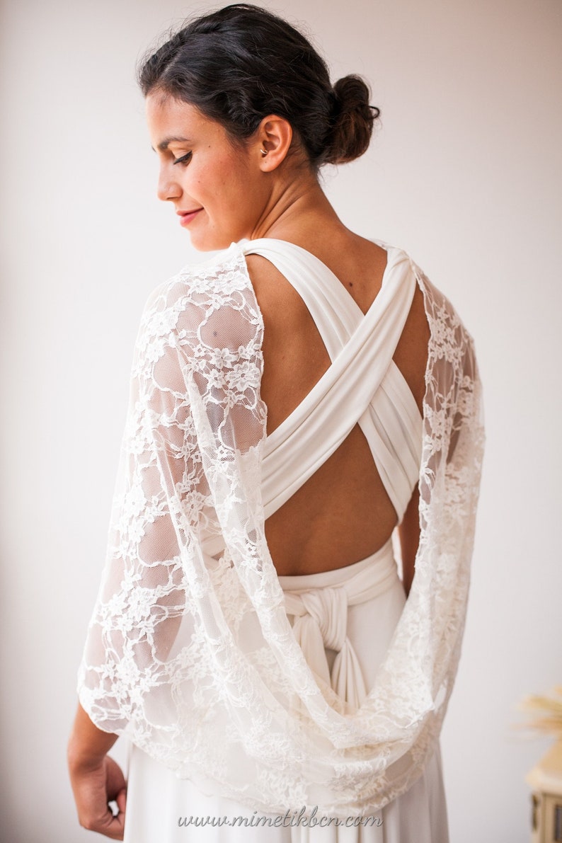 May include: A white dress featuring a crisscross back design and a sheer white lace shawl draped over the shoulders. The dress has a tied waist detail at the back. The text www.mimetikbcn.com is visible at the bottom of the image.
