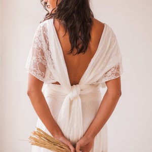 We see a back close-up of a woman wearing a wedding dress. She wears a bouquet in her hands. The room has abundance of natural light. She looks both beautiful and confortable in her alternative bridal dress. The wedding gown is convertible.