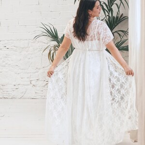 May include: A white lace wedding dress with a flowing skirt and a V-neckline. The dress has short sleeves and a fitted bodice.