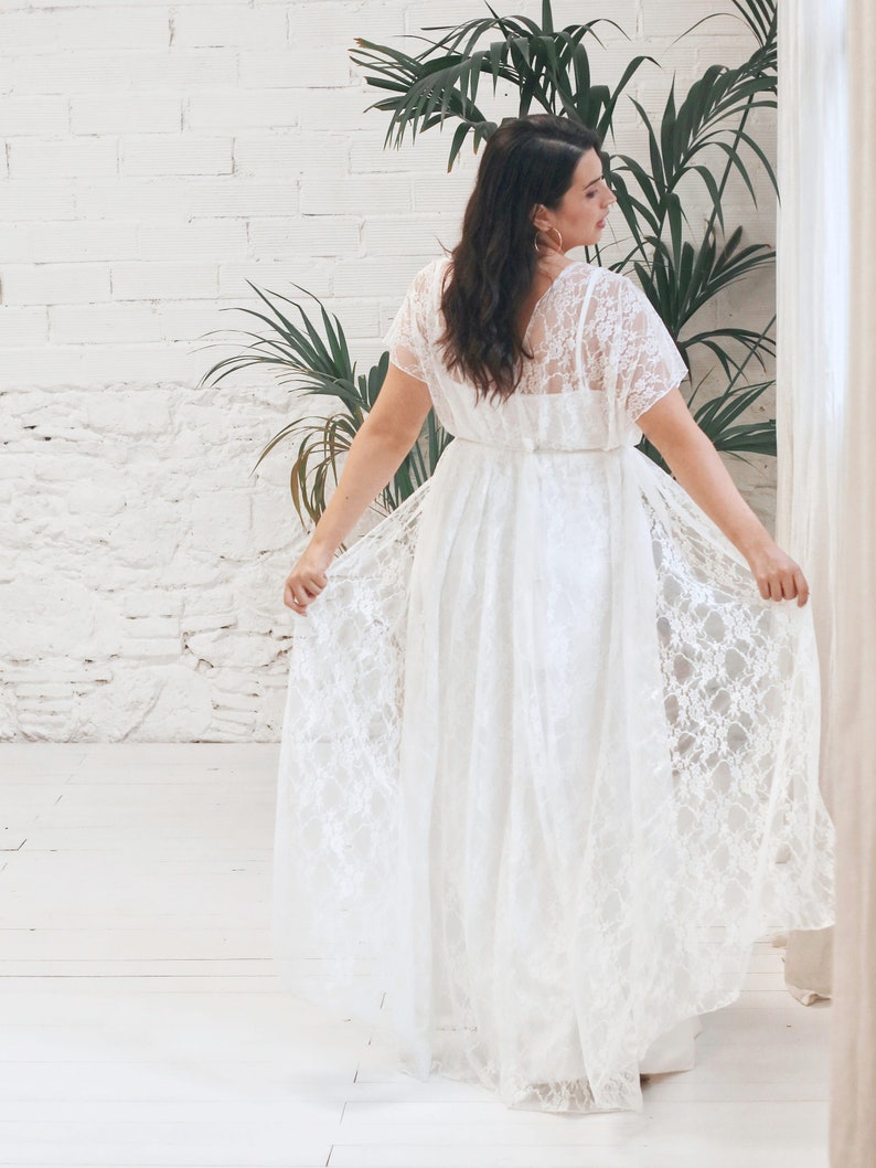 May include: A white lace wedding dress with a flowing skirt and a V-neckline. The dress has short sleeves and a fitted bodice.