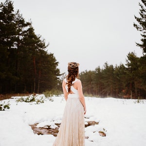 Bride in a snowy landscape. It looks beautiful and calm as only snow can be. She is in the middle, between two rows of trees. Her boho bridal gown is perfect for an elopement