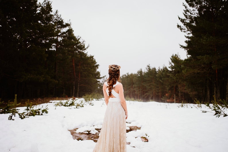 Bride in a snowy landscape. It looks beautiful and calm as only snow can be. She is in the middle, between two rows of trees. Her boho bridal gown is perfect for an elopement