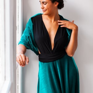May include: A floor-length dress featuring a deep black V-neck bodice with a wide waistband and a flowing teal velvet skirt. The garment includes a matching teal velvet shawl draped over the shoulders, creating a cohesive and elegant ensemble.