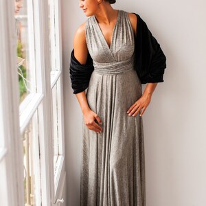 May include: A floor-length metallic silver wrap dress with a V-neckline and a gathered waist, paired with a black velvet shrug. The dress features a sleeveless bodice with wide straps and a flowing, floor-length skirt with subtle vertical texture.
