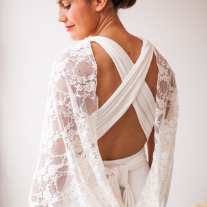 May include: A white dress featuring a crisscross back design and a sheer white lace shawl draped over the shoulders. The dress has a tied waist detail at the back. The text www.mimetikbcn.com is visible at the bottom of the image.
