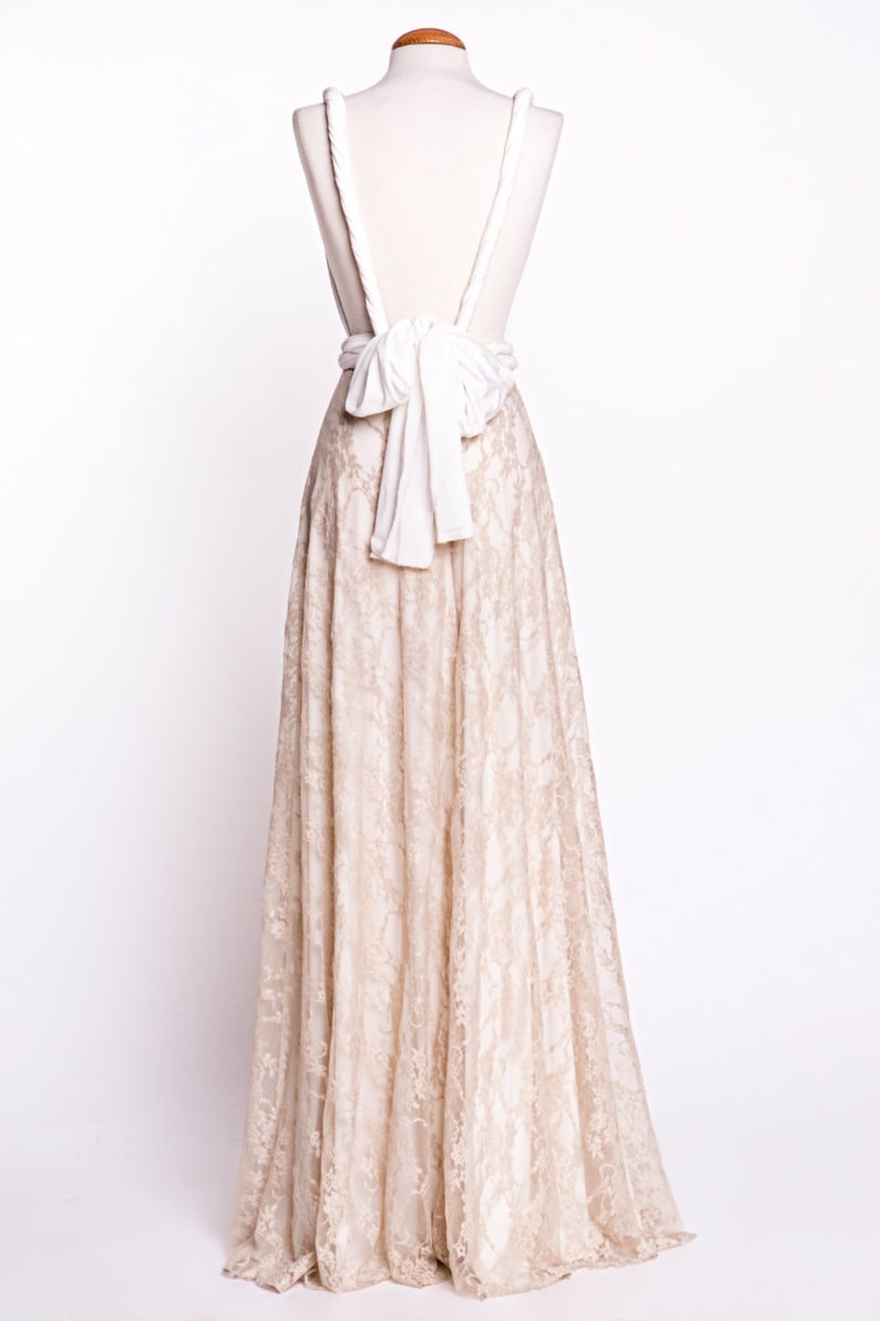 May include: A floor-length dress featuring a beige lace skirt and a solid white bodice. The back of the garment displays thick white straps that cross and secure with a large, prominent white fabric bow at the waistline, creating an open-back design.