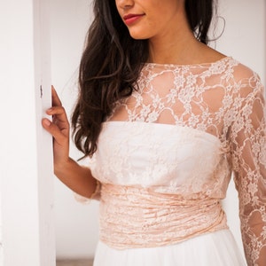 Close-up of a boho bride. She has a romantic smile. The close-up shows in detail a pink lace bodice with long sleeves. The bodice is a wrap.