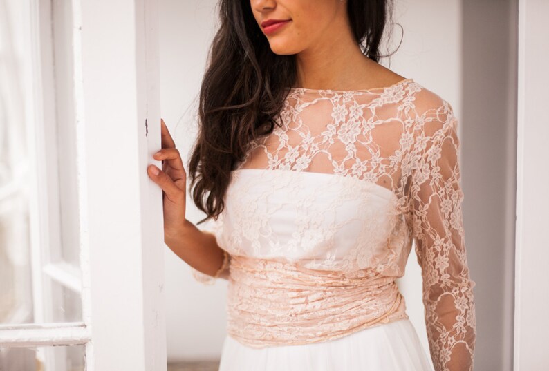 Close-up of a boho bride. She has a romantic smile. The close-up shows in detail a pink lace bodice with long sleeves. The bodice is a wrap.