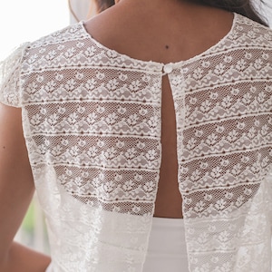 May include: White lace top with a keyhole back and a button closure. The top has a delicate floral pattern and is sleeveless.