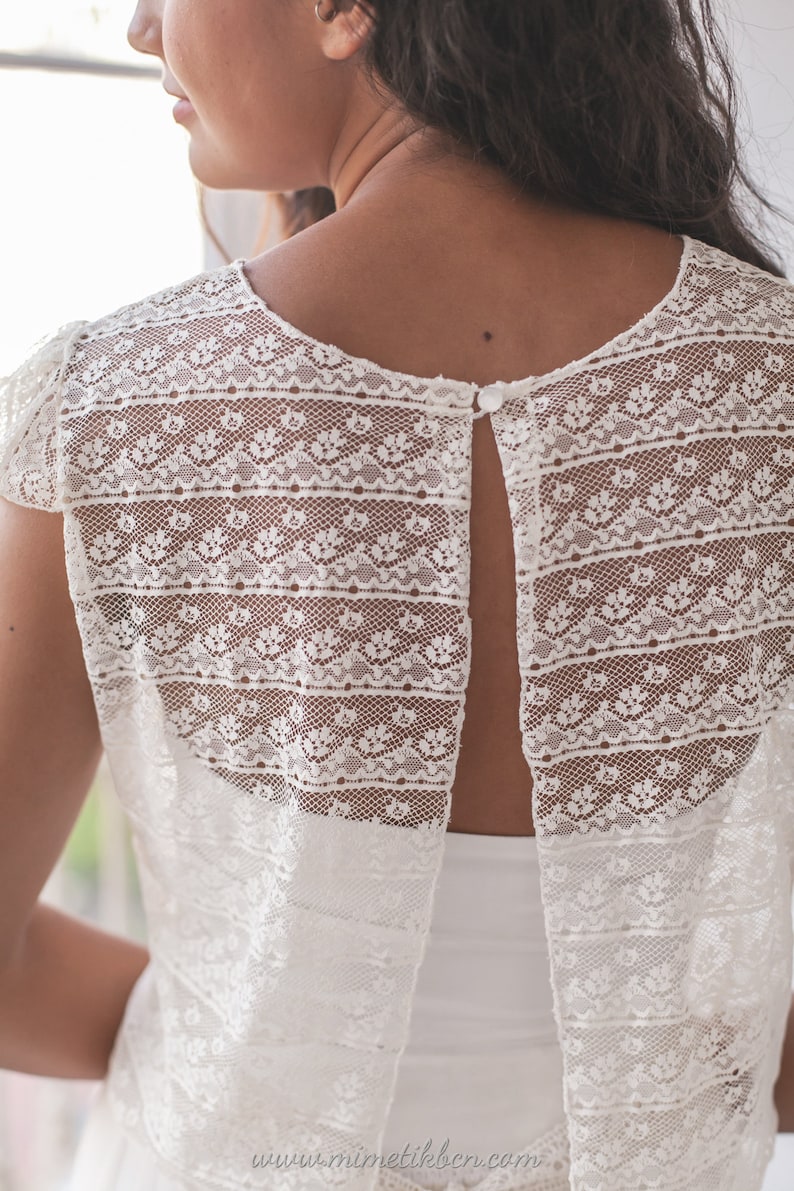 May include: White lace top with a keyhole back and a button closure. The top has a delicate floral pattern and is sleeveless.