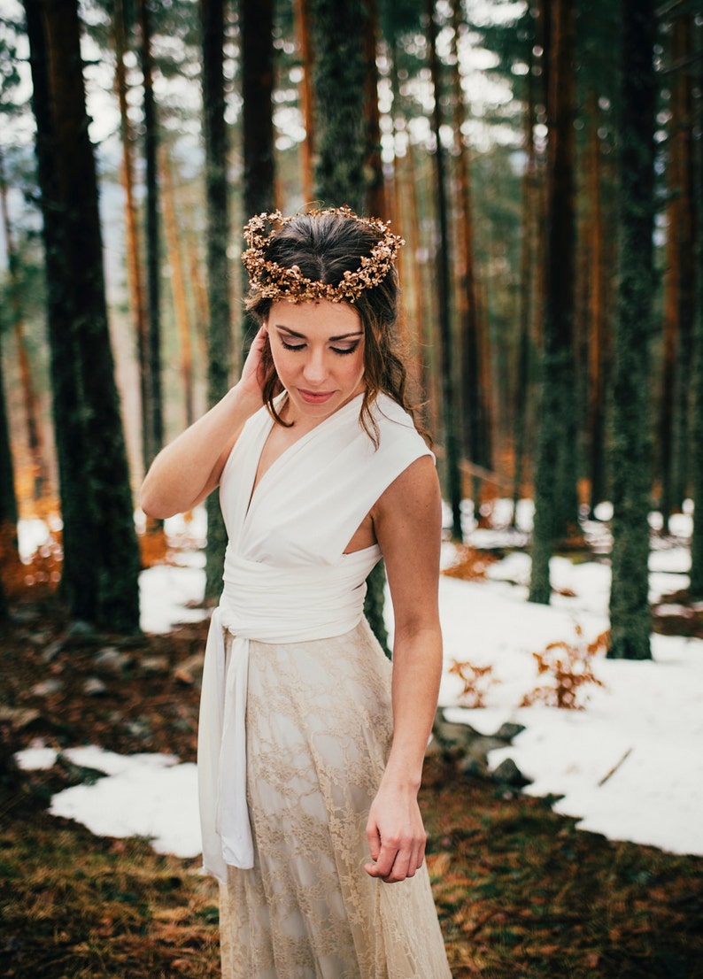 Woman wearing a fall wedding gown in the woods. It's a bit snowy. The woman is wearing a flowery headband that combines perfectly with her bridal gown in ivory and golden