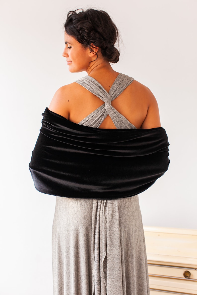 May include: A black velvet wrap shawl draped horizontally across the shoulders and upper back, featuring a soft, light-reflecting texture. The wrap is worn over a heather gray sleeveless dress with wide, crossed straps at the upper back.