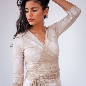 Brunette model touching her hair. She is wearing a golden beige lace wedding with v-neck and long sleeves