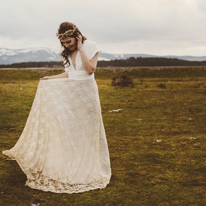 Incredible photo of a bride in a beautiful natural landscape. It's all green and there are some snowy mountains in the background. She is smiling and showing her boho wedding dress. It's easy to imagine that she is a rustic bride