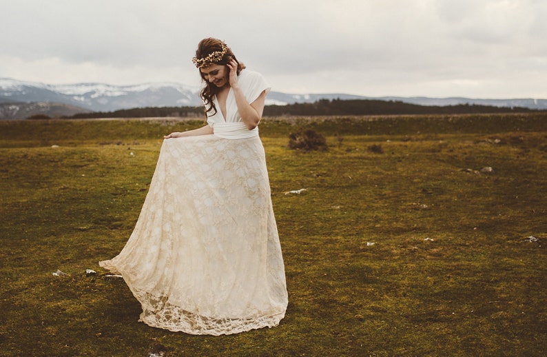 Incredible photo of a bride in a beautiful natural landscape. It's all green and there are some snowy mountains in the background. She is smiling and showing her boho wedding dress. It's easy to imagine that she is a rustic bride