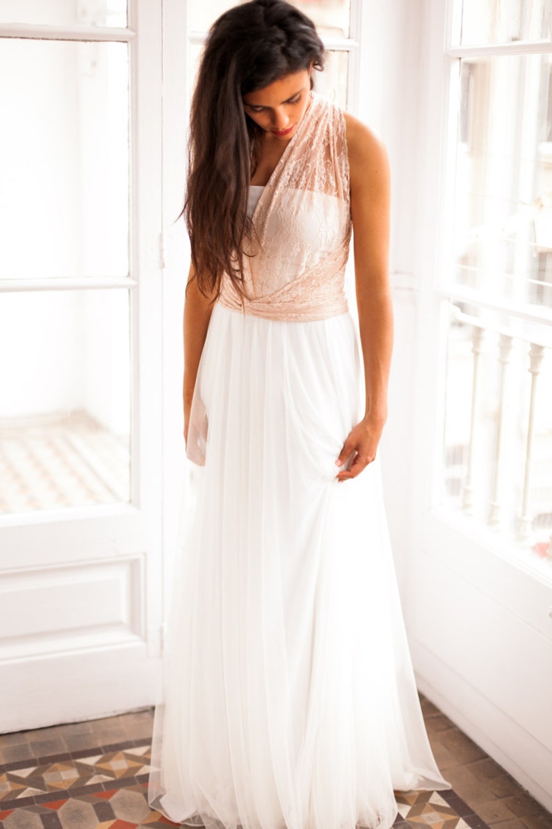 Model standing in a corner of a luminous room. She is in front of a glass door and next to a big window. She looks romantic and vintage in her boho wedding dress.