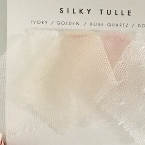 May include: A display card labeled SILKY TULLE featuring four fabric swatches in ivory, golden, rose quartz, and a white dotted pattern. The text on the card lists the colors as IVORY / GOLDEN / ROSE QUARTZ / DOTTED, showcasing the sheer mesh texture.