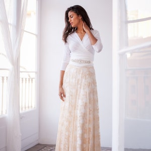 This time the woman is wearing a three-quarter sleeved wedding dress, but this time with a golden lace overskirt and a shimmer vintage belt. The viewer sees her standing up next to a window.