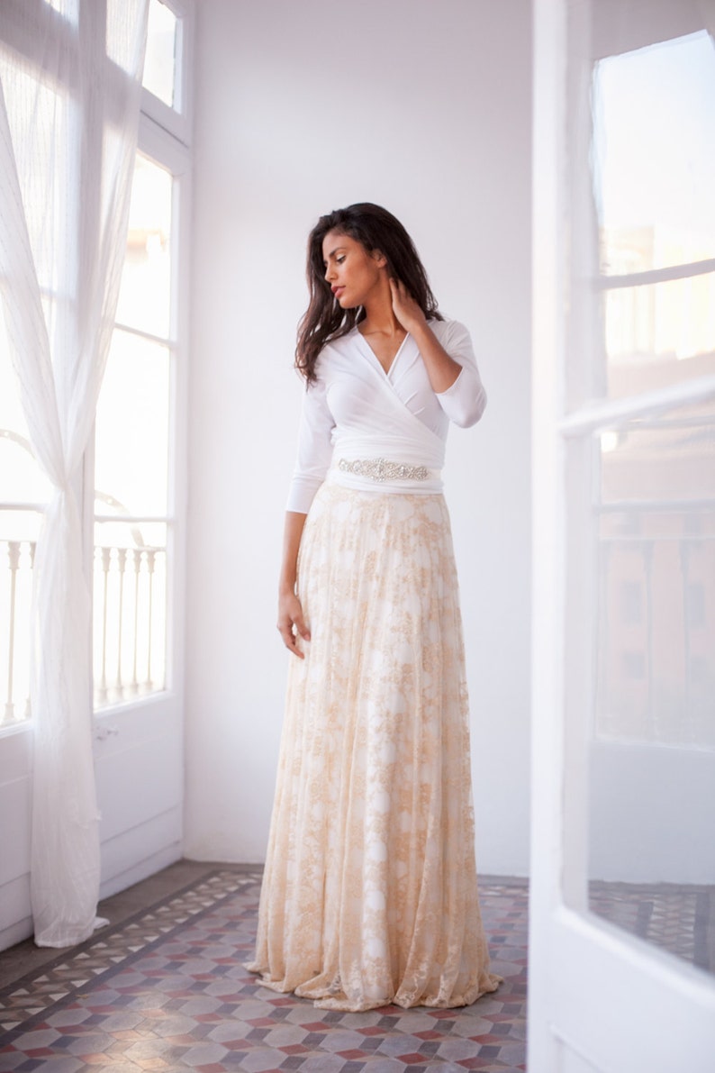 This time the woman is wearing a three-quarter sleeved wedding dress, but this time with a golden lace overskirt and a shimmer vintage belt. The viewer sees her standing up next to a window.