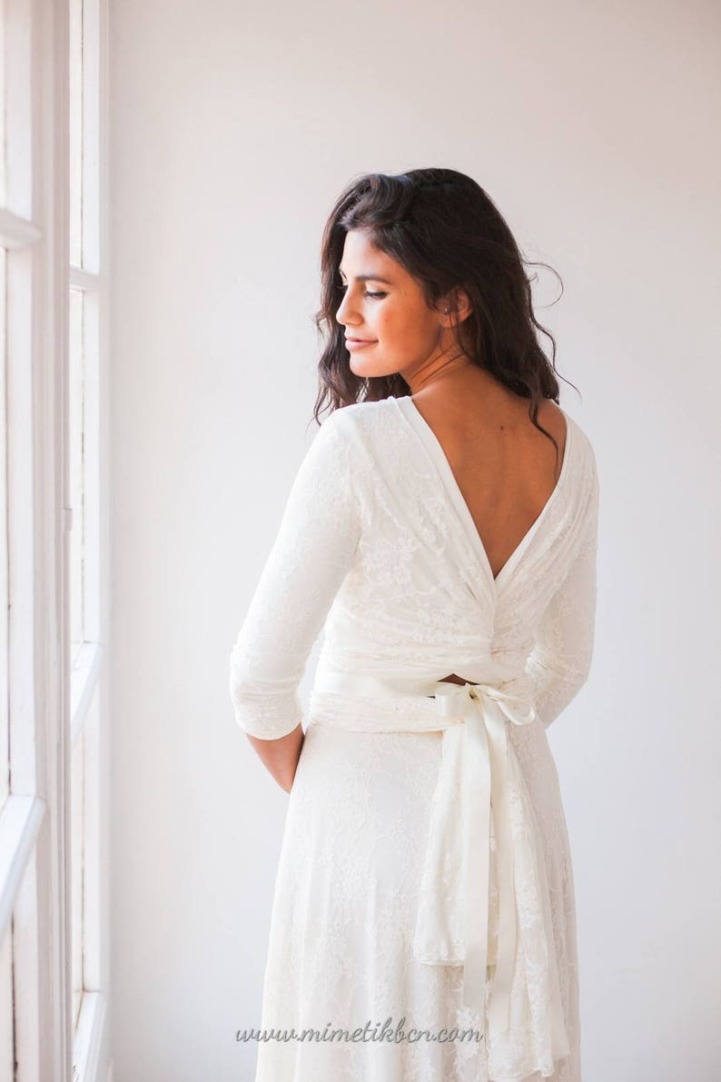 Model dressed like a bride standing up in a room and showing the back of her bridal gown. The bolero is wrapped in the waist and is easily shown.