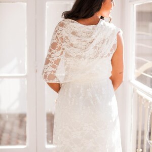 The model is showing her back to the viewer while looking outside. She is wearing a tight sexy dress with a ivory lace overdress.