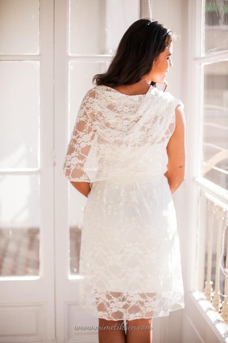 The model is showing her back to the viewer while looking outside. She is wearing a tight sexy dress with a ivory lace overdress.