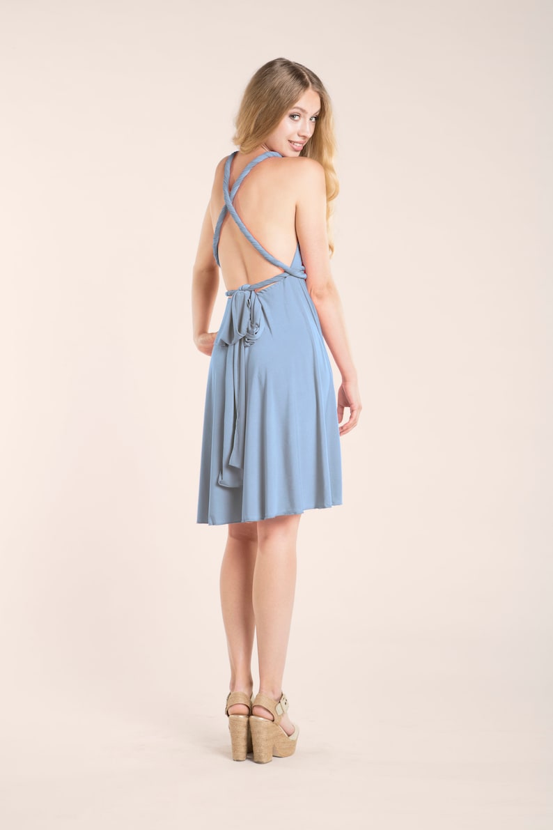 May include: A dusty blue knee-length dress featuring a backless design with twisted straps that cross over the shoulders and a tie closure at the waist. The garment has a flared skirt and a smooth, solid-colored fabric construction throughout.