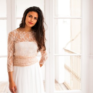 Bride looking at the camera with a romantic smile. She is wearing a bridal gown made of lace (in the cover-up) and tulle (in the overskirt). She has a beautiful long hair, with no accessories, perfect for a boho bride