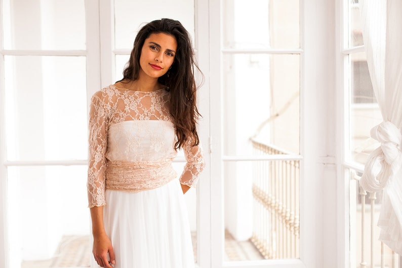 Bride looking at the camera with a romantic smile. She is wearing a bridal gown made of lace (in the cover-up) and tulle (in the overskirt). She has a beautiful long hair, with no accessories, perfect for a boho bride