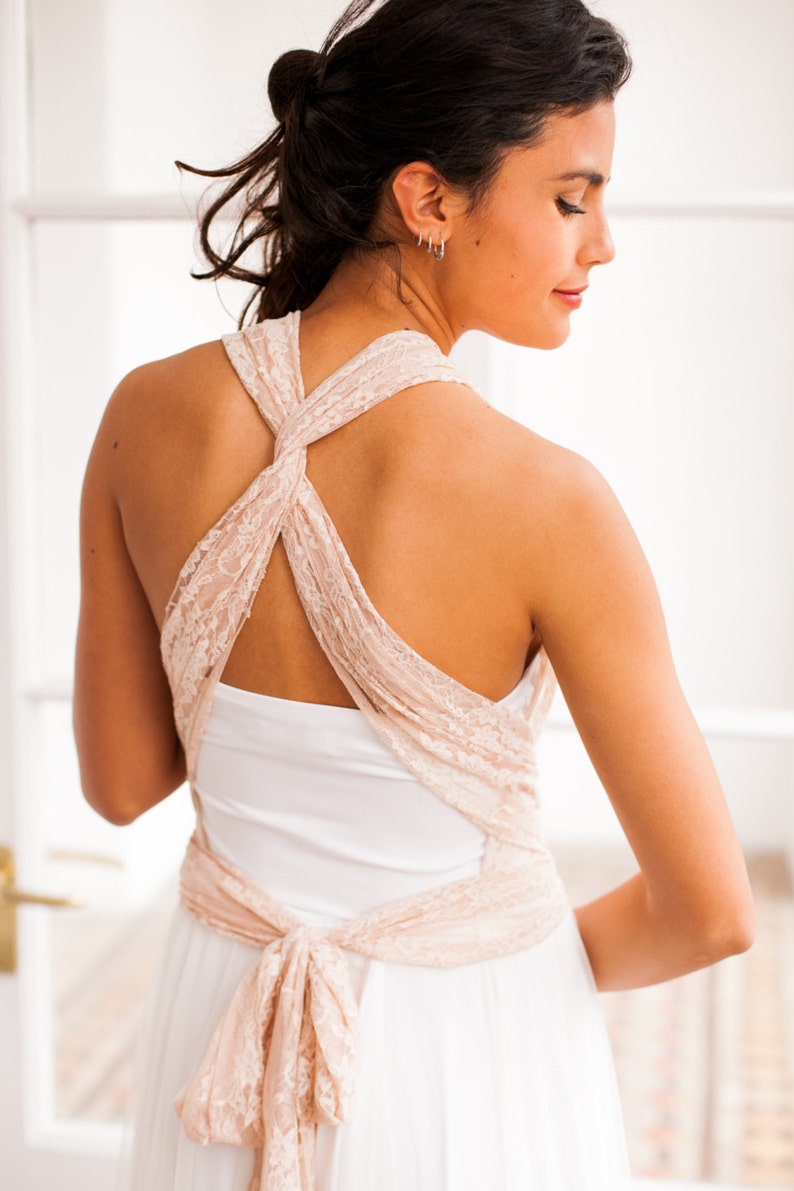 Close-up of a model wearing a bridal gown. This combines a long skirt, a tulle overskirt, a tube top, and convertible straps in pink lace. The straps are crossed on her back but this is not the only way to wear it, as it's a convertible dress