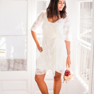 The woman is wearing now a short bridal lace overdress. The viewer can see her long legs and peep-toe shoes.