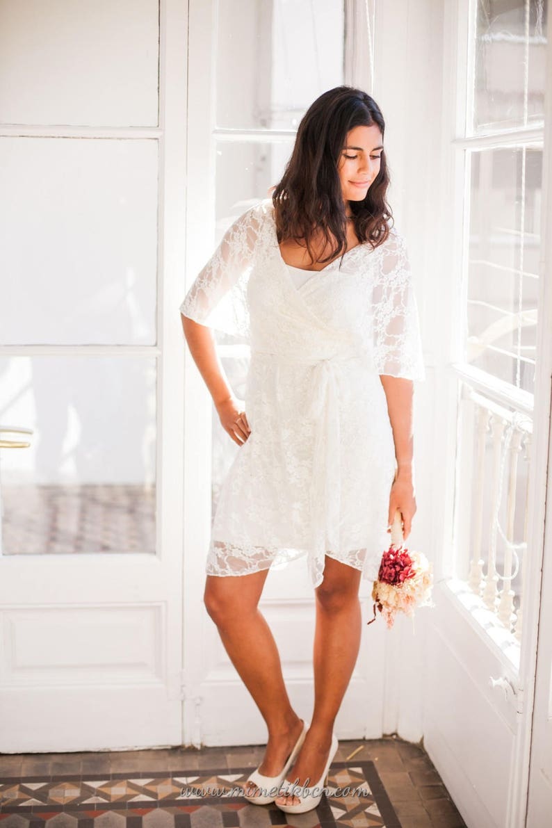 The woman is wearing now a short bridal lace overdress. The viewer can see her long legs and peep-toe shoes.